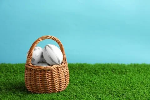 Wicker basket of painted Easter eggs on green lawn against color background,  스톡 사진