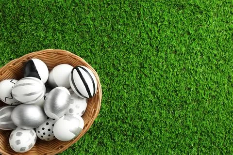 Wicker basket of painted Easter eggs on green lawn, top view with space for t 写真素材