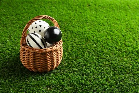Wicker basket of painted Easter eggs on green lawn, space for text 写真素材