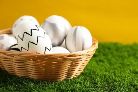 Wicker basket of painted Easter eggs on green lawn against color background,  Stock Photos