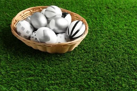 Wicker basket of painted Easter eggs on green lawn, space for text 写真素材