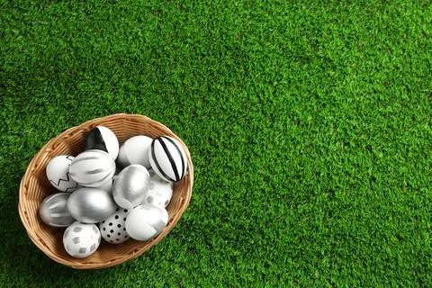 Wicker basket of painted Easter eggs on green lawn, top view with space for t 写真素材