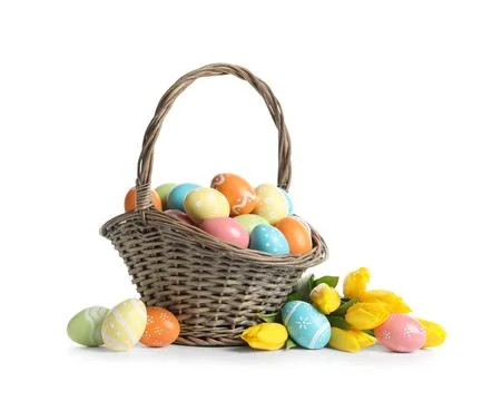 Wicker basket with painted Easter eggs and spring flowers on white background Stock Photos