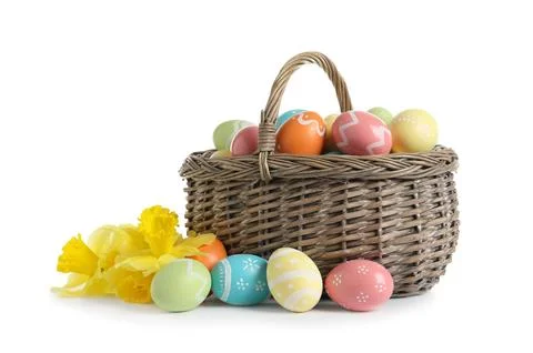 Wicker basket with painted Easter eggs and spring flowers on white background Foto stock