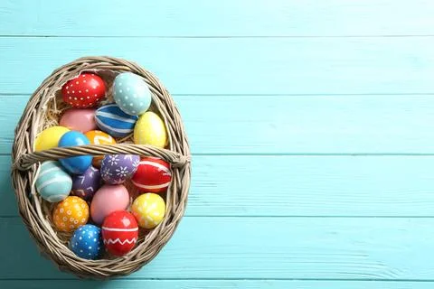 Wicker basket with painted Easter eggs on wooden background, top view. Space  스톡 사진