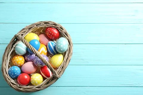 Wicker basket with painted Easter eggs on wooden background, top view. Space  Stock Photos
