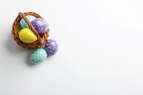 Wicker basket with painted Easter eggs on white background, top view Stock Photos
