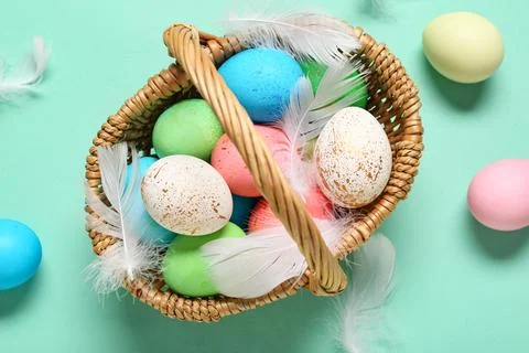 Wicker basket with painted Easter eggs and feathers on turquoise background Stock Photos