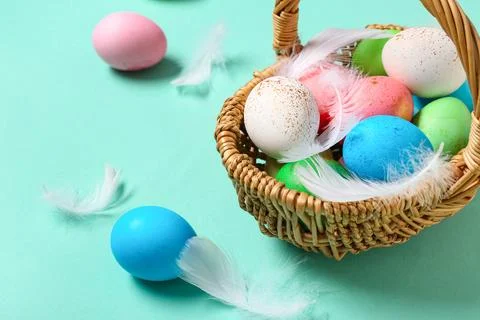 Wicker basket with painted Easter eggs and feathers on turquoise background Stock Photos