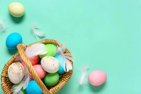 Wicker basket with painted Easter eggs and feathers on turquoise background Stock Photos