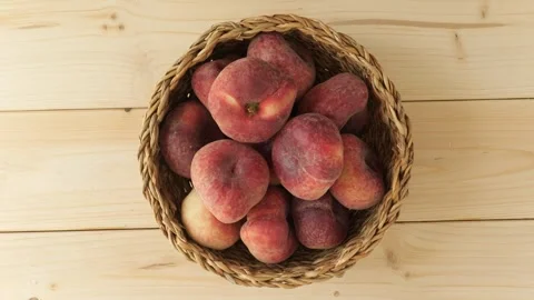 Wicker basket of ripe peaches rotating on wooden background Stock Footage 343435562