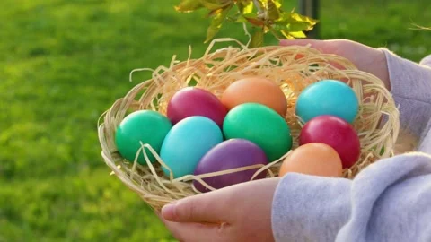 Wicker basket with straw and Easter eggs in childs hands in spring garden Stock Footage 302294957