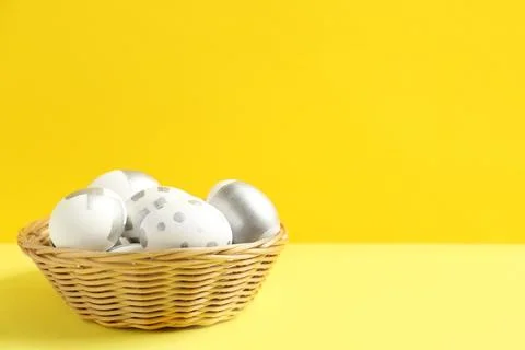 Wicker bowl of Easter eggs on table against color background. Space for text Stock Photos