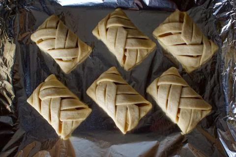 Wicker buns with an apple on a baking sheet. Raw buns. Stock Photos
