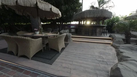 Wicker dining set and thatched tiki bar on a backyard patio Stock Footage 345544282