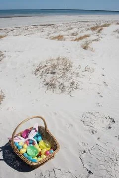 Wicker Easter basket with toy easter eggs and bunny ears at beach Stock Photos
