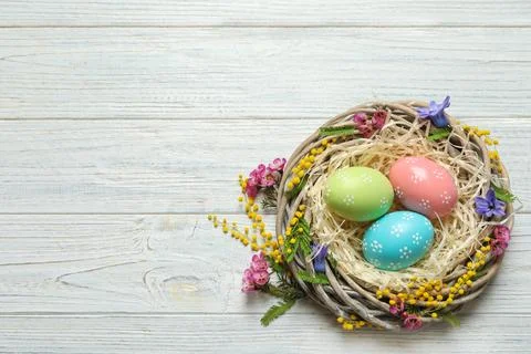 Wicker nest with painted Easter eggs and flowers on wooden table, top view. S Fotos de archivo