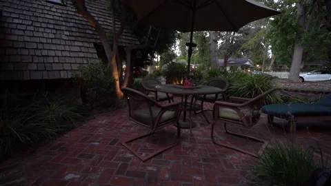 Wicker patio dining set under an umbrella on a brick terrace at dusk Stock Footage 345530441