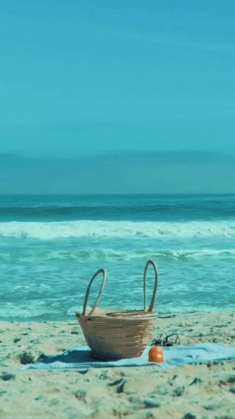 Wicker picnic basket on sandy beach with ocean waves in background Stock Footage 342572780