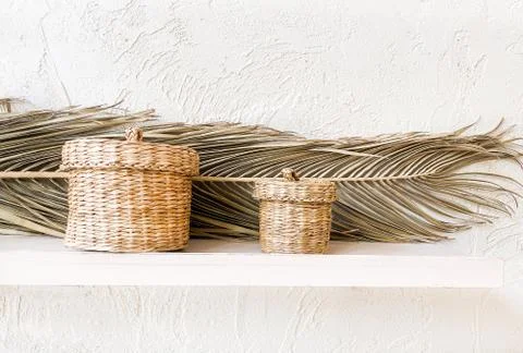 Wicker straw decorative baskets on white shelves with dry palm leaves. Stock Photos