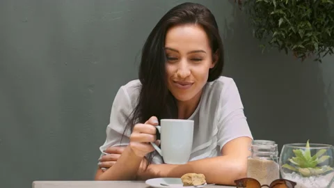 Wide 4k video of a young, beautiful, Latin Hispanic woman drinking coffee in gar Видео 201096942