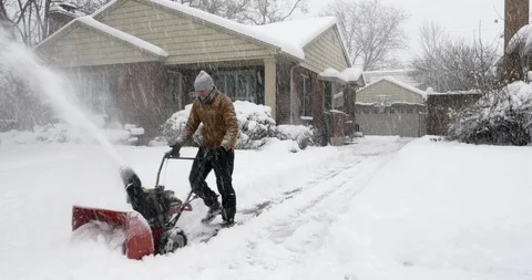 Wide-angle of man operating snow blower at his house during winter storm. Video stock 124333418