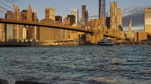 Wide angle of Manhattan skyline lit by rising sun, reflecting as waves crash Stock Footage 99093404
