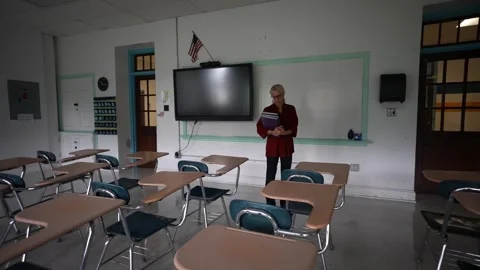 Wide angle push in view of sad teacher in an empty classroom with the lights Stock Footage 245123541