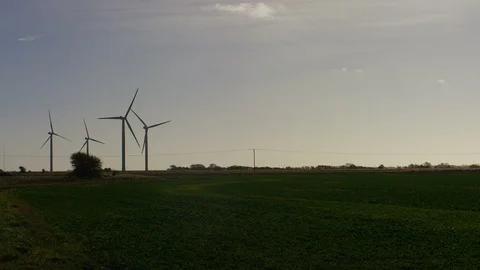 Wide angle shot of 3 out of 4 wind turbines rotating in the distance at sundown Stock Footage 98066710