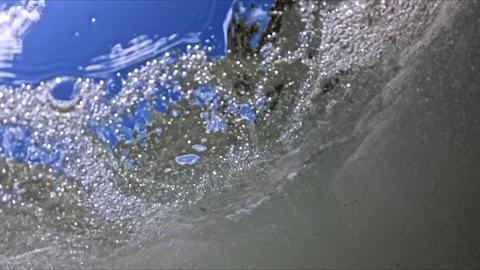 Wide-angle shot of foamy waves hitting rocks under bright sun, camera dips .. Video stock 313876022