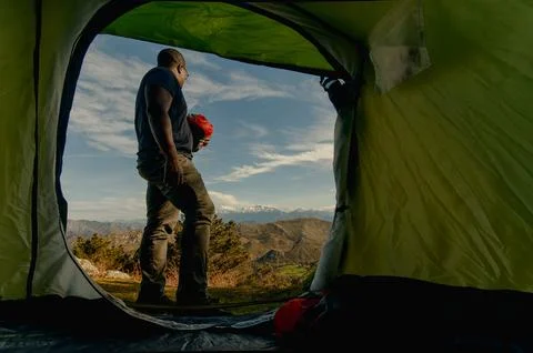Wide-angle shot from inside the green tent of black male camper standing outside Foto stock