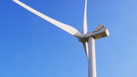 Wide-Angle Shot of a Wind Turbine Rotating Against a Clear Blue Sky 動画素材 296931041
