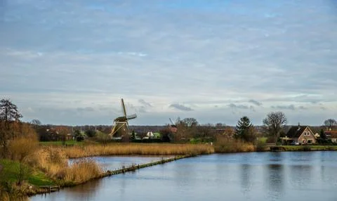 A wide angle shot of a windmill surrounded by trees and greenery in front of  Stock Photos