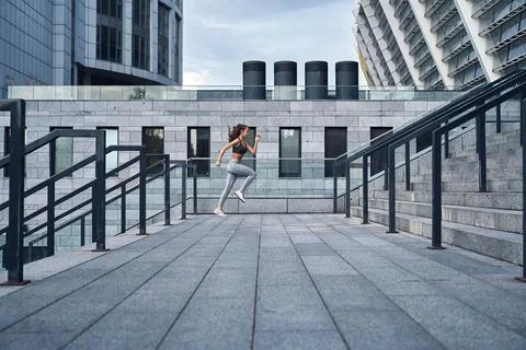 Wide angle shot of young athletic woman running upstairs, jumping training at Stock Photos