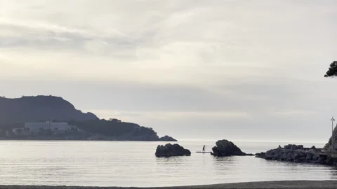 Wide angle sunset beach view with a human figurine paddling on stand up paddle S Stock-Footage 283983954