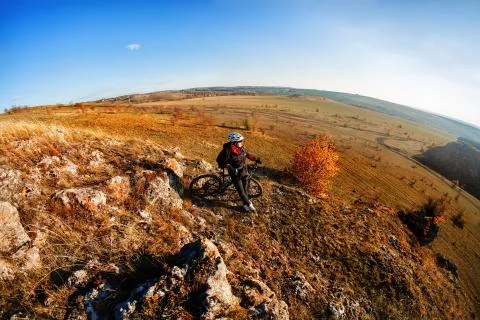 Wide angle view of cyclist standing with mountain bike on trail at sunset. Stock Photos