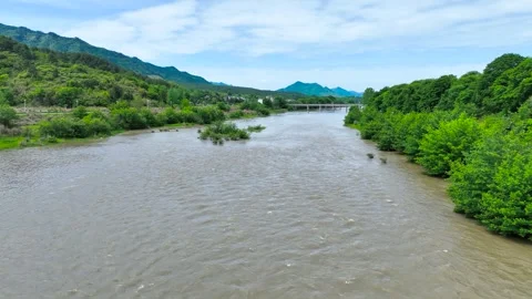 Wide angle view of a muddy river flowing through a lush green valley Vídeos de archivo 342237367