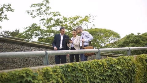 Wide angle view of three coworkers looking at digital tablet while walking down Stock Footage 277974264