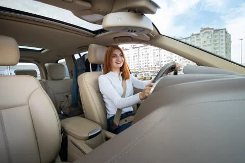 Wide angle view of young redhead woman driver fastened by seatbelt driving a  Stock Photos