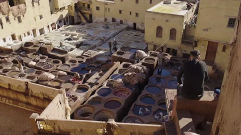 Wide back shot of boy looking at tannery workers dyeing leather in Fes Stock Footage 265456398