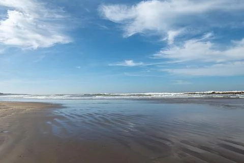 Wide beach under soft blue sky with scattered clouds Stock Photos