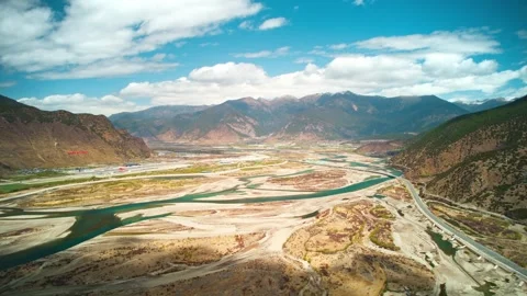 Wide braided river floodplain and valley road beneath blue sky in Tibet Video stock 345884339