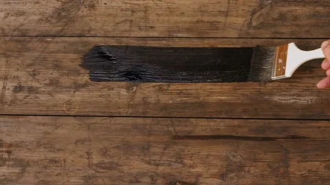 A wide brush in a man's hand covers a wooden surface with a dark varnish 库存影片 209595038