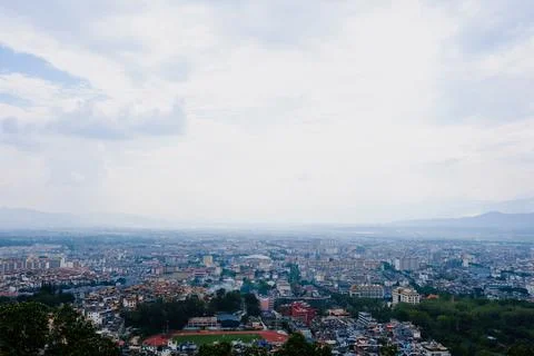 Wide city view under cloudy sky from hillside Stock Photos