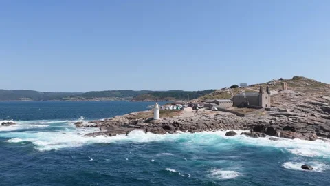 Wide daytime view of the Faro de Muxia lighthouse on a rugged rocky coastline Stock Footage 346705948