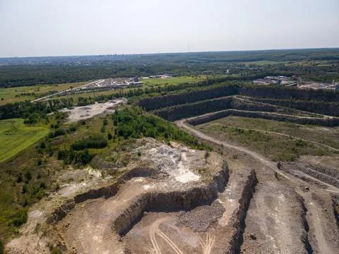 Wide drone shot captures massive terraced open pit granite quarry with dirt r Fotos Stock