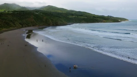 Wide drone shot of a cloudy New Zealand beach with surfers and horse riders Stock Footage 89892109