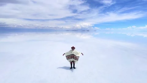 Wide Drone Shot of Man in Hat and Poncho Standing on Uyuni Salt Flats Video stock 337264442