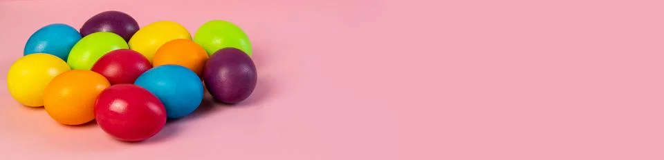 Wide Easter banner empty. Multi-colored eggs on a pink background. Stock Photos