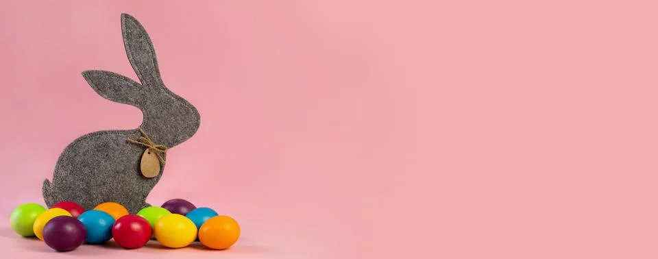 Wide Easter banner. Gray hare and eggs are multi-colored on a pink background. Stock Photos